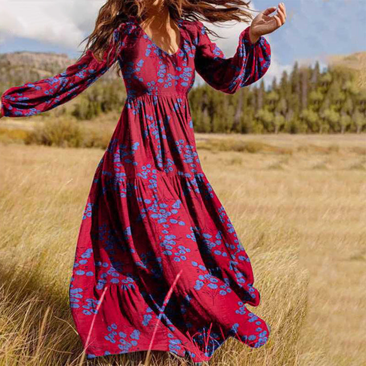 Woman in a red floral dress standing in a field with trees and sky in the background