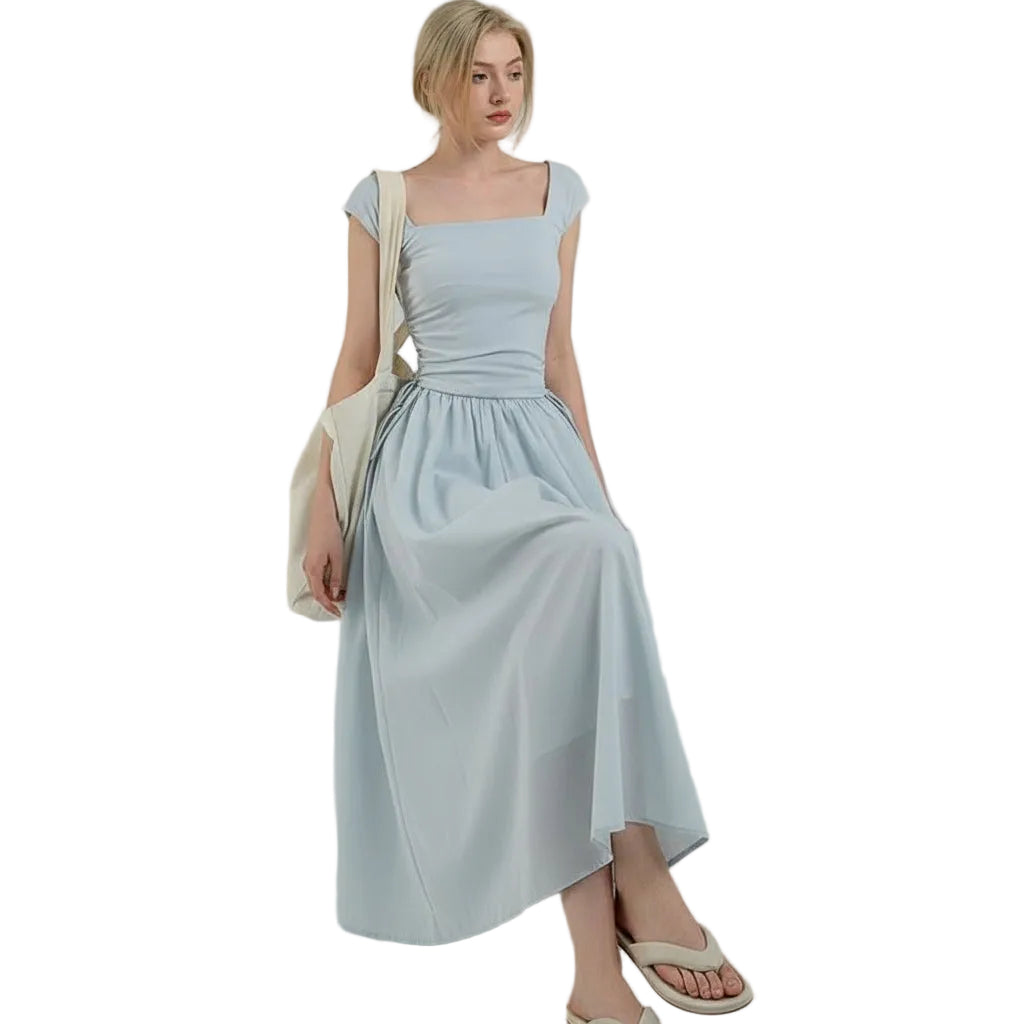 Woman in a light blue dress standing outdoors with a bench and wall in the background